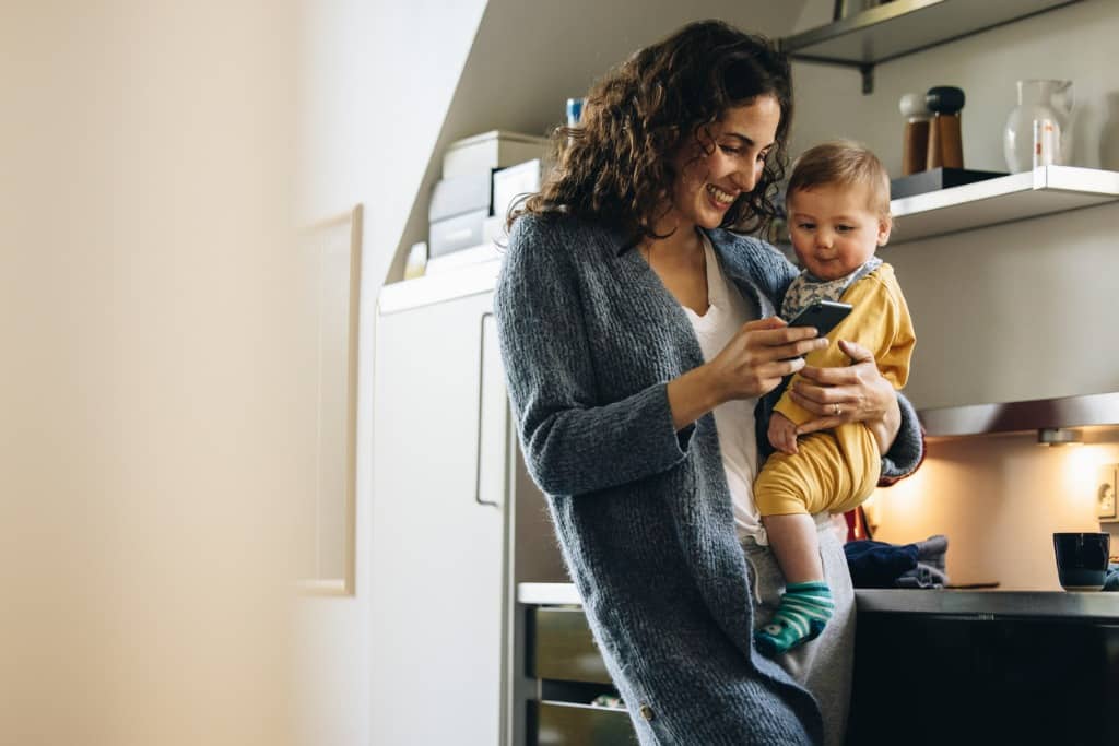 smiling woman with baby texting on phone at home picture id1314404449